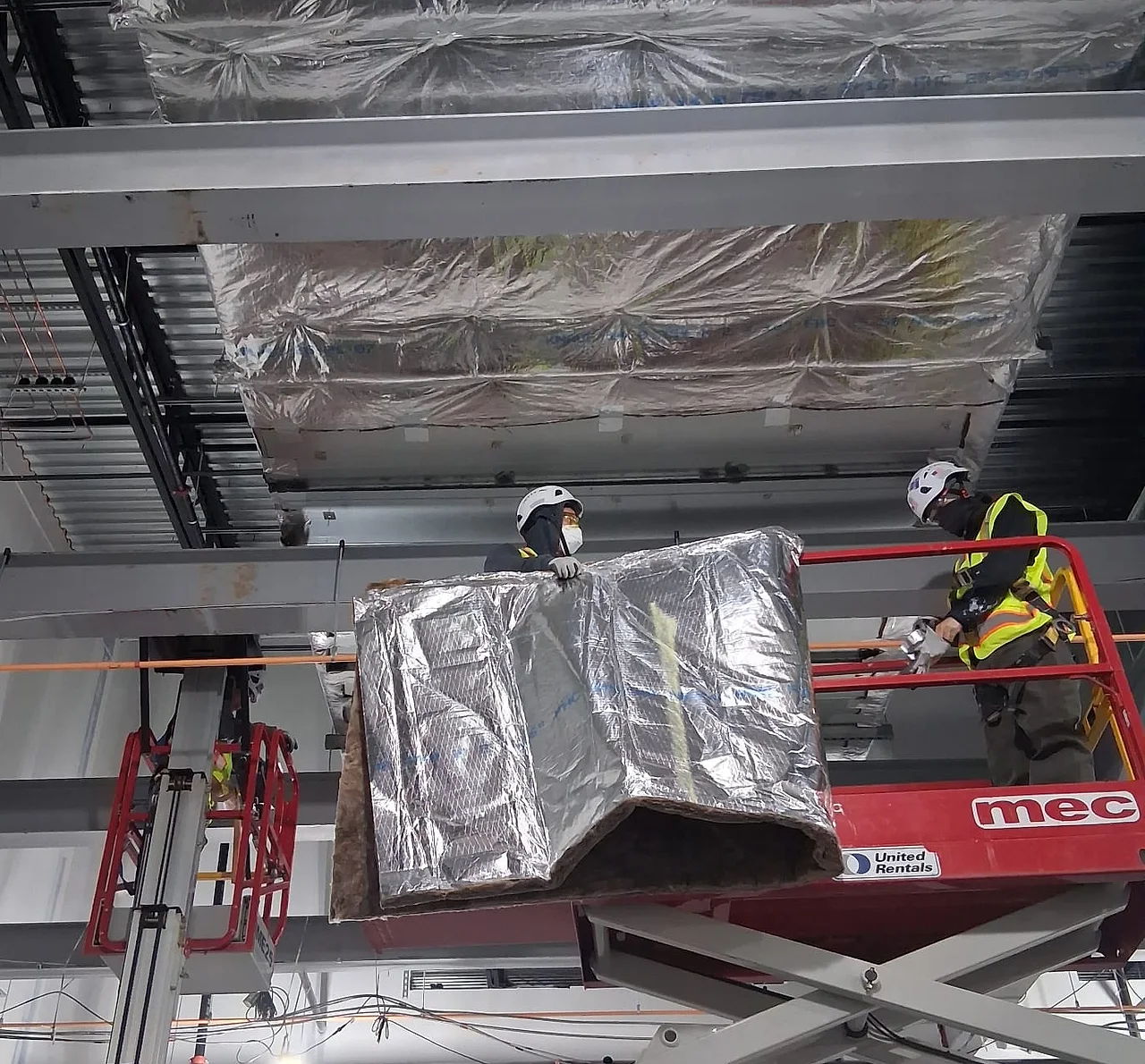 Cuadrilla de Sabaoth FQ izando un tramo de ducto forrado en foil desde un elevador dentro de un edificio comercial